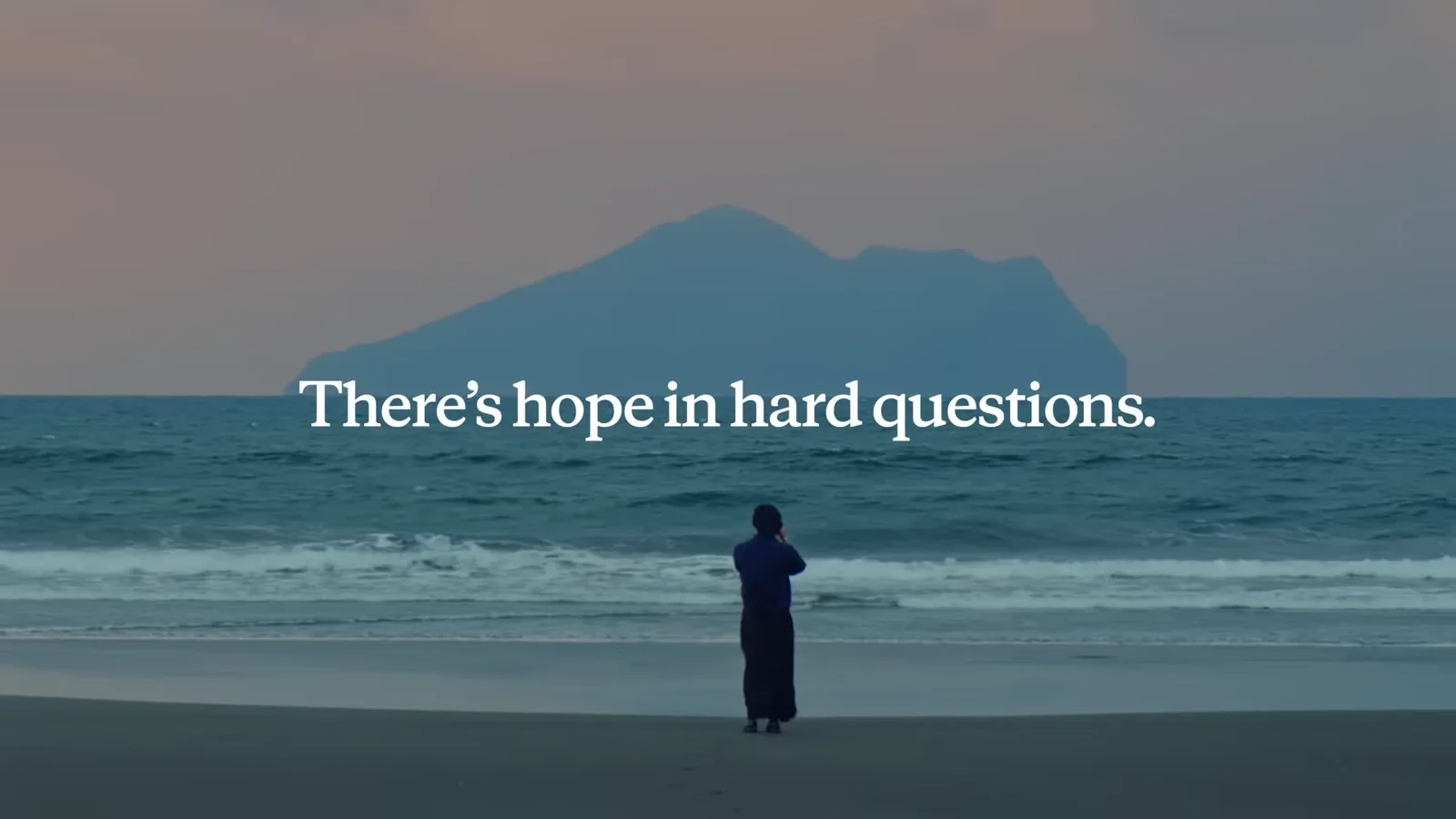 影片片尾字卡:「There's hope in hard questions.」壓在龜山島鏡頭上——暮色中一人站在黑沙灘望向海中的龜山島(影片畫面:Anthropic《There's hope in hard questions》,YouTube @claude)